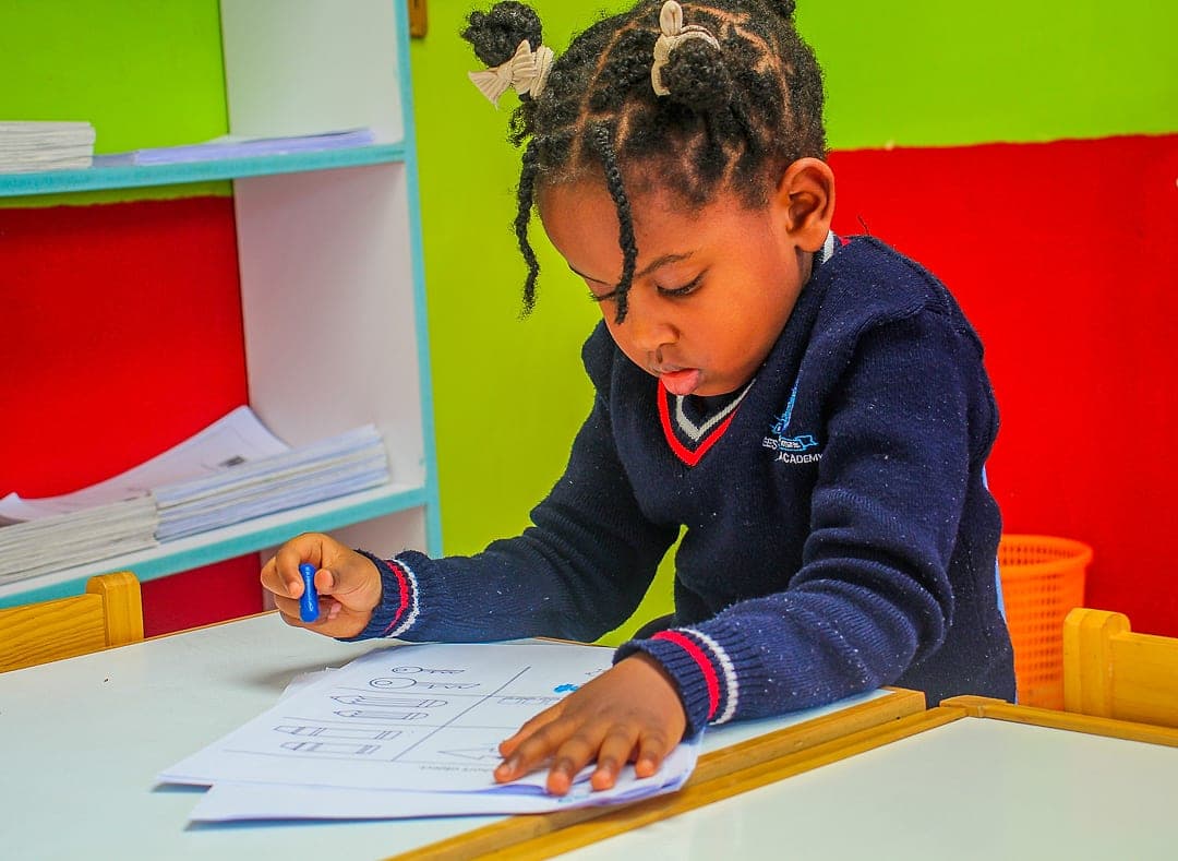 A young child in school uniform tracing letter shapes on a worksheet