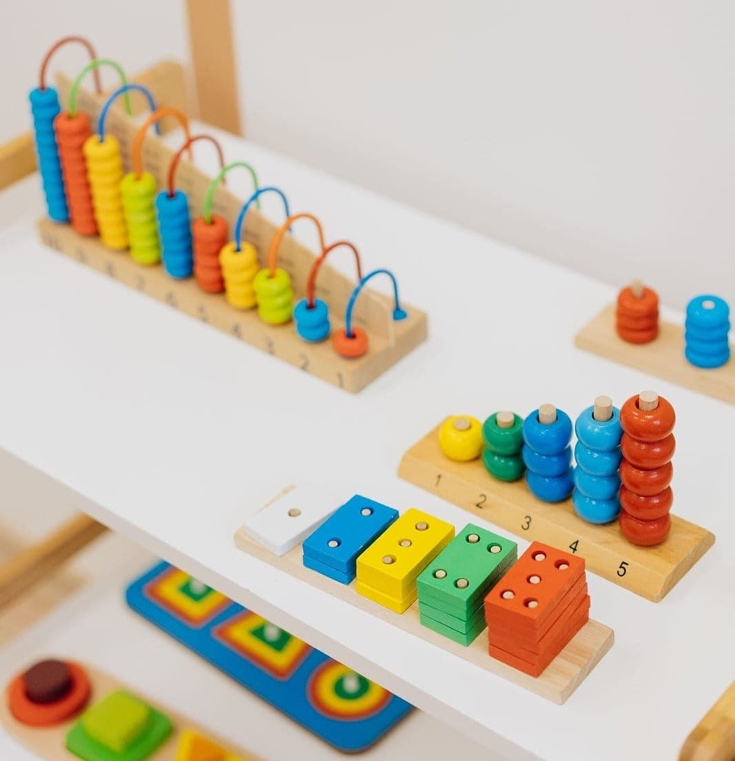 A wooden counting frame, numbered bead stacks and dotted number blocks laid out on a low open shelf