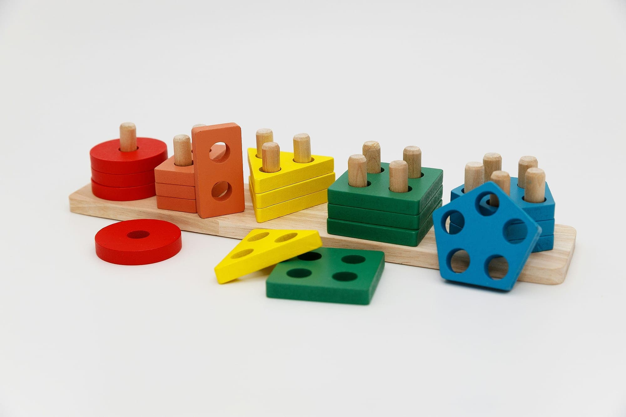 A wooden shape sorter with coloured discs, triangles, squares and pentagons stacked on pegs