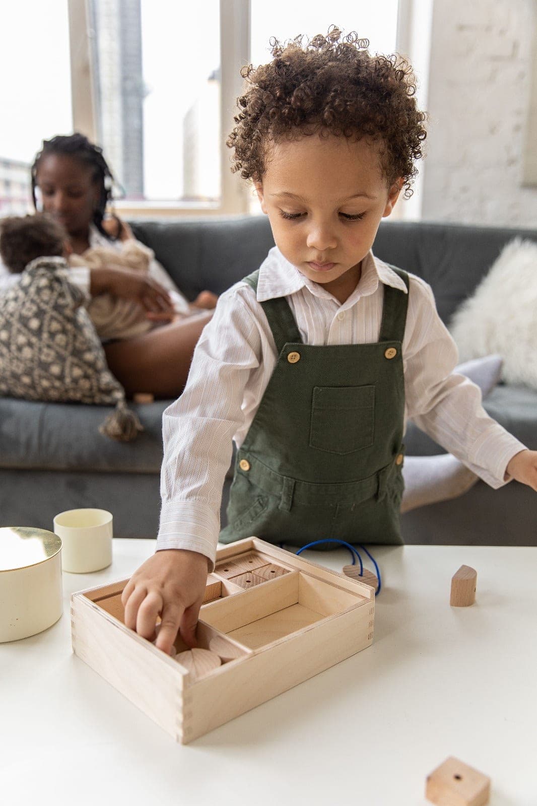 A toddler in green dungarees picking a wooden shape out of a Montessori sorting box
