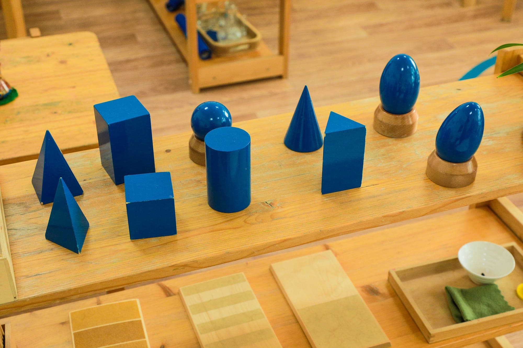 Blue Montessori geometric solids lined up on a wooden shelf